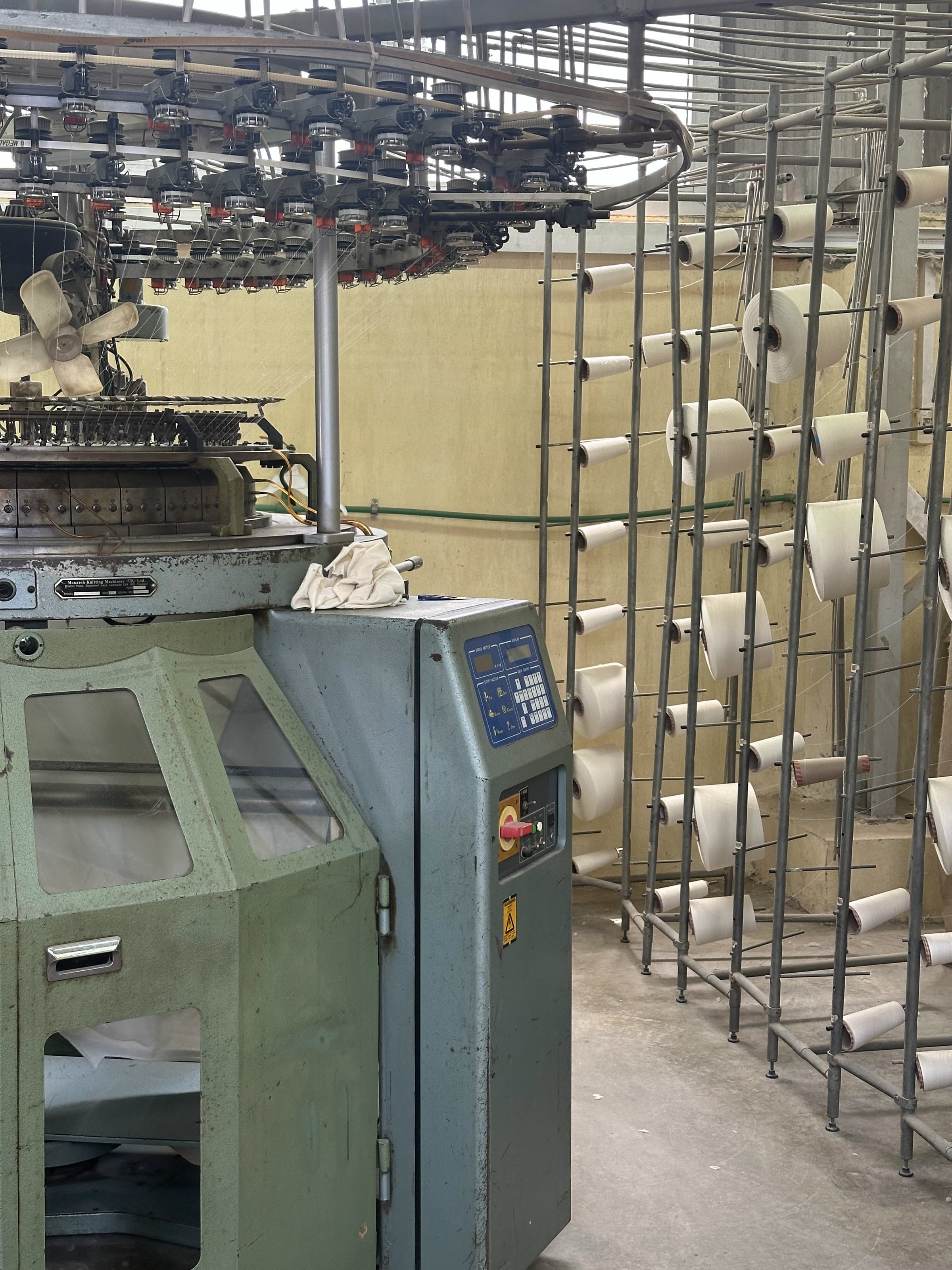 A circular knitting machine beside a creel of cotton yarn cones